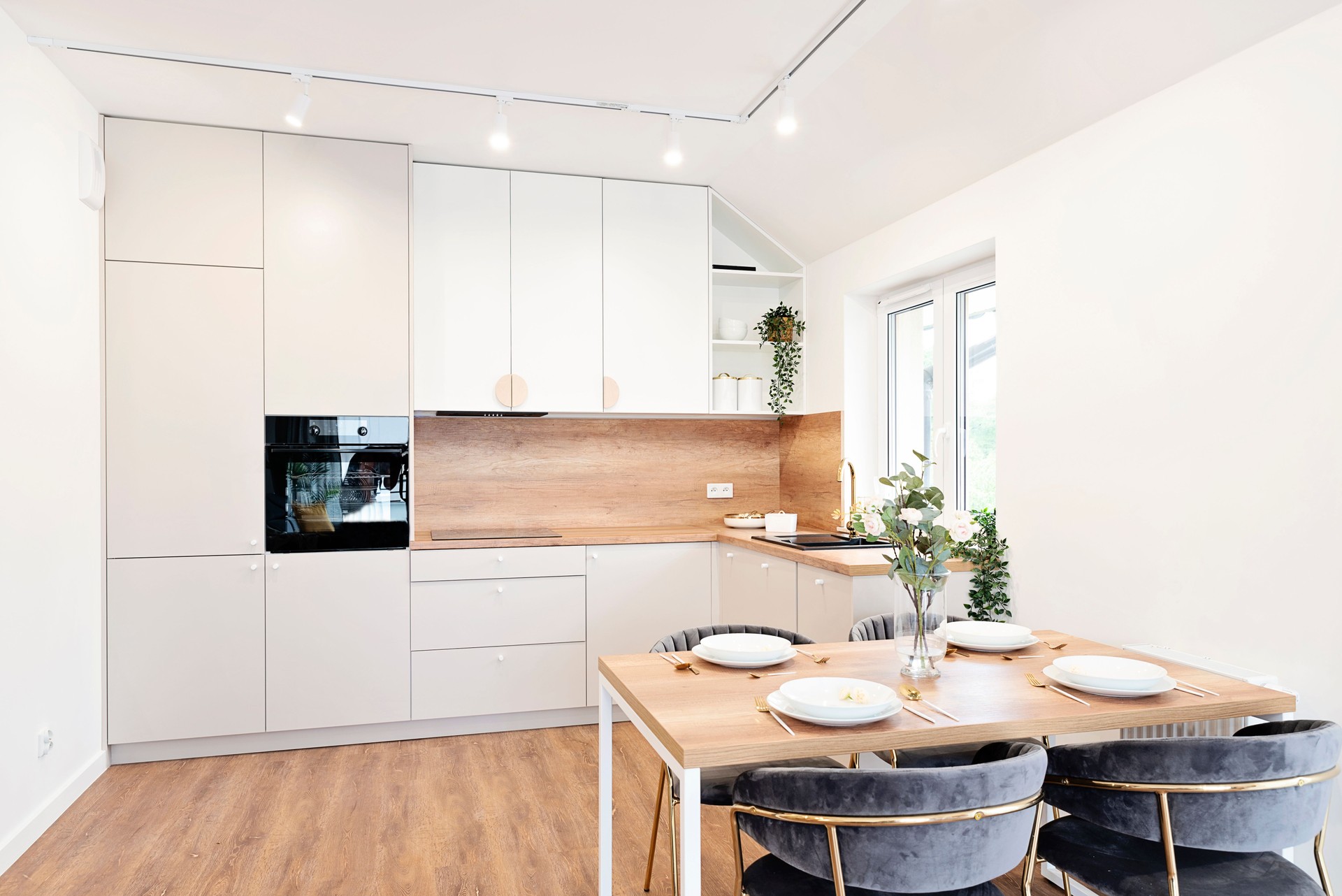 Modern interior of kitchen with furniture and dining table, wooden counter and kitchen sink with water tap. Window with plant and new design in apartment. Real estate.