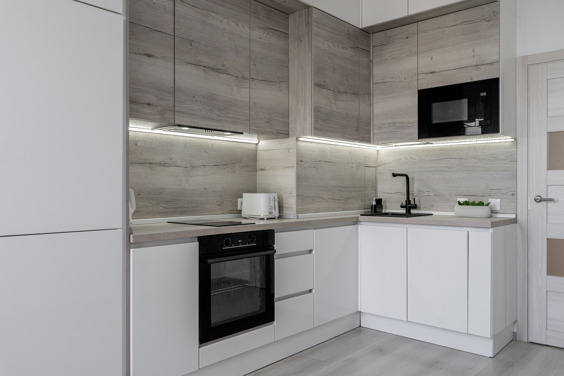 interior of modern apartment. design of built-in kitchen with white cabinets and black countertops. kitchen is clean and bright. perfect order. minimalist kitchen design with cabinets and backsplash.
